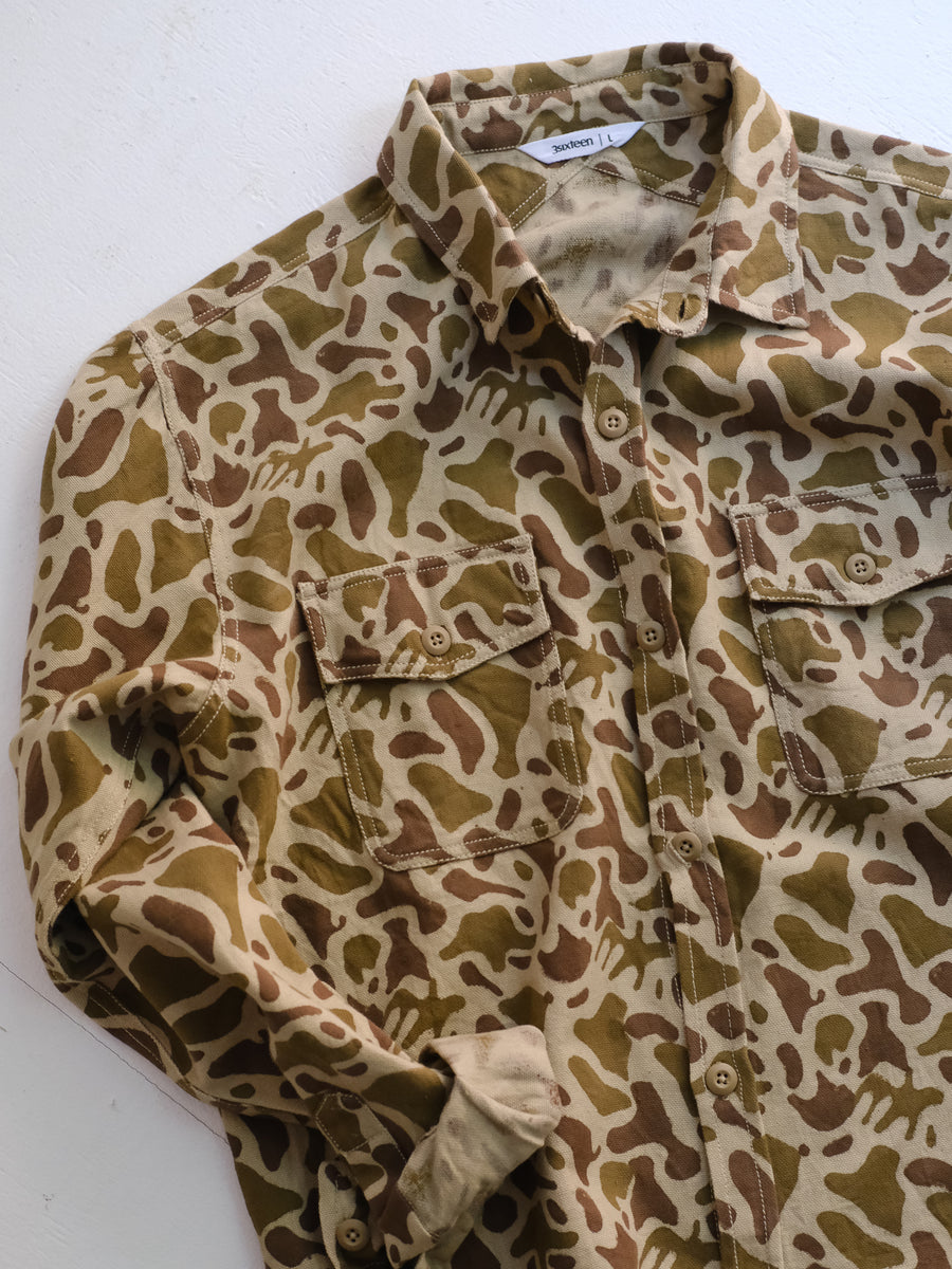 A shot of a camouflage shirt with rolled sleeves on the floor.