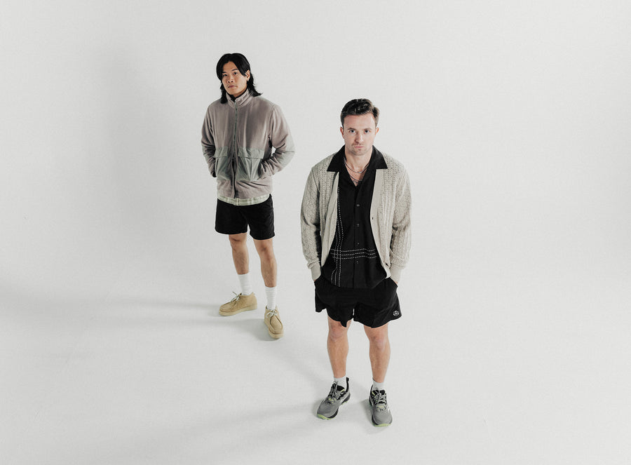 Two men pose in grey tops and black shorts.