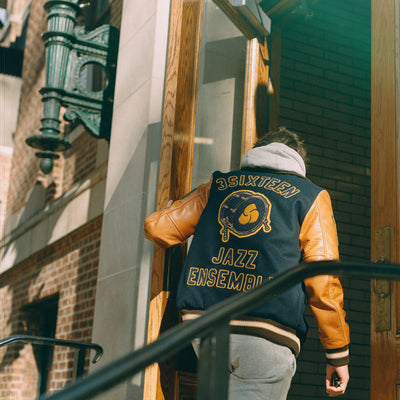 A man in a navy varsity jacket walks into a classroom door.