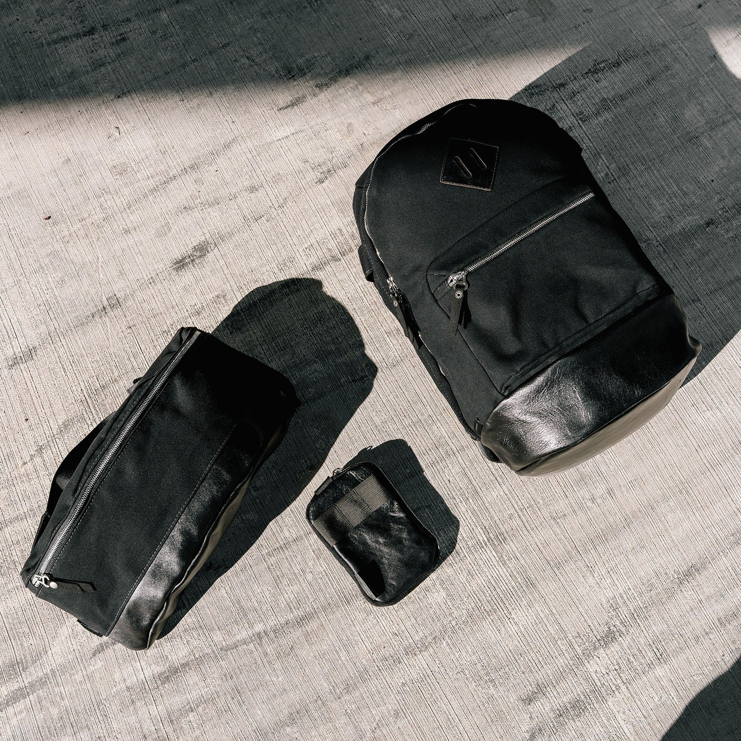A trio of black canvas bags with black leather bottoms on a concrete floor.