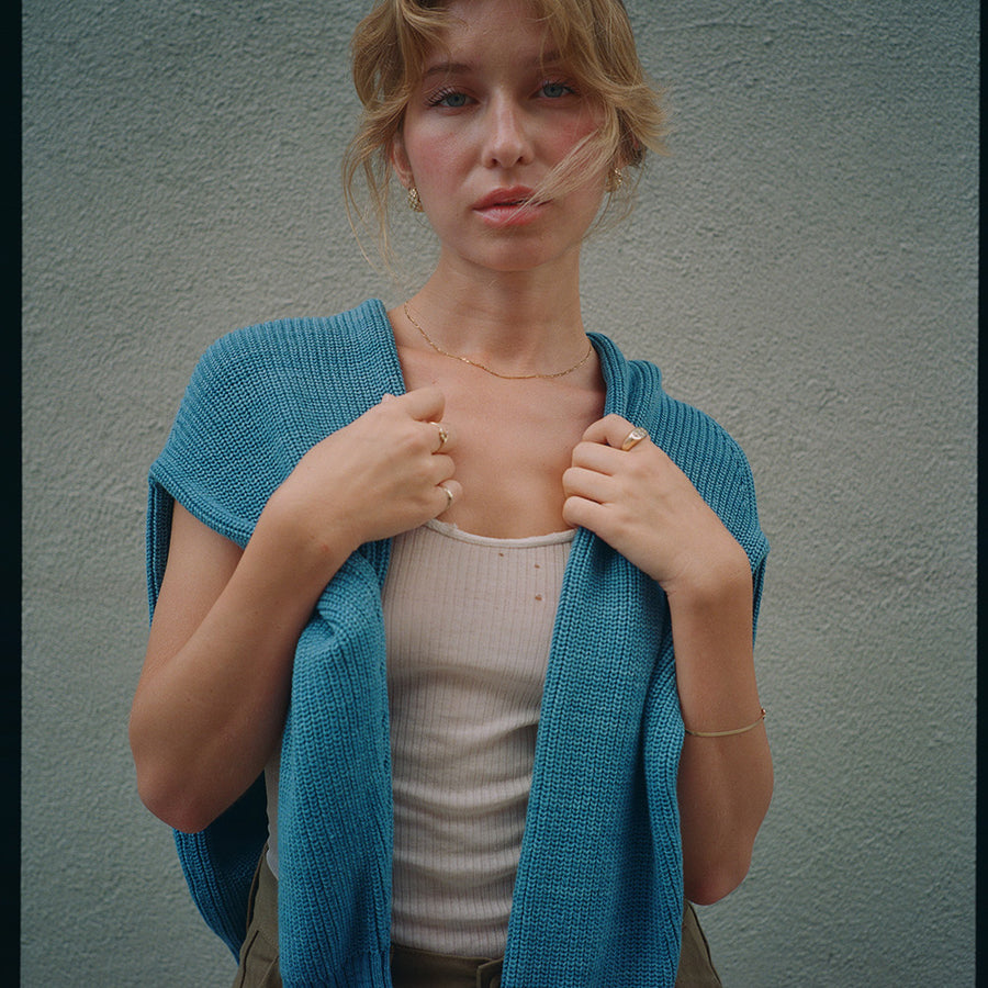 A woman in a blue sweater stands in front of a grey wall