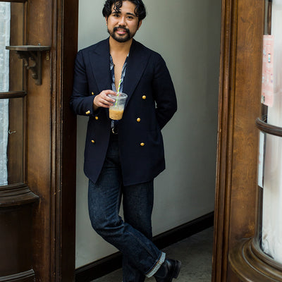 A man holds an iced coffee and stands in a doorway.