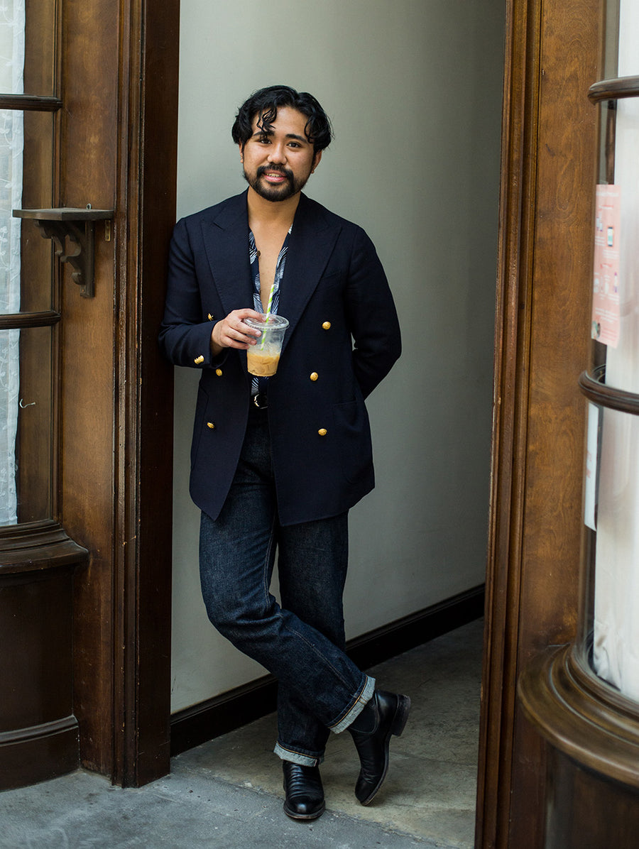 A man holds an iced coffee and stands in a doorway.