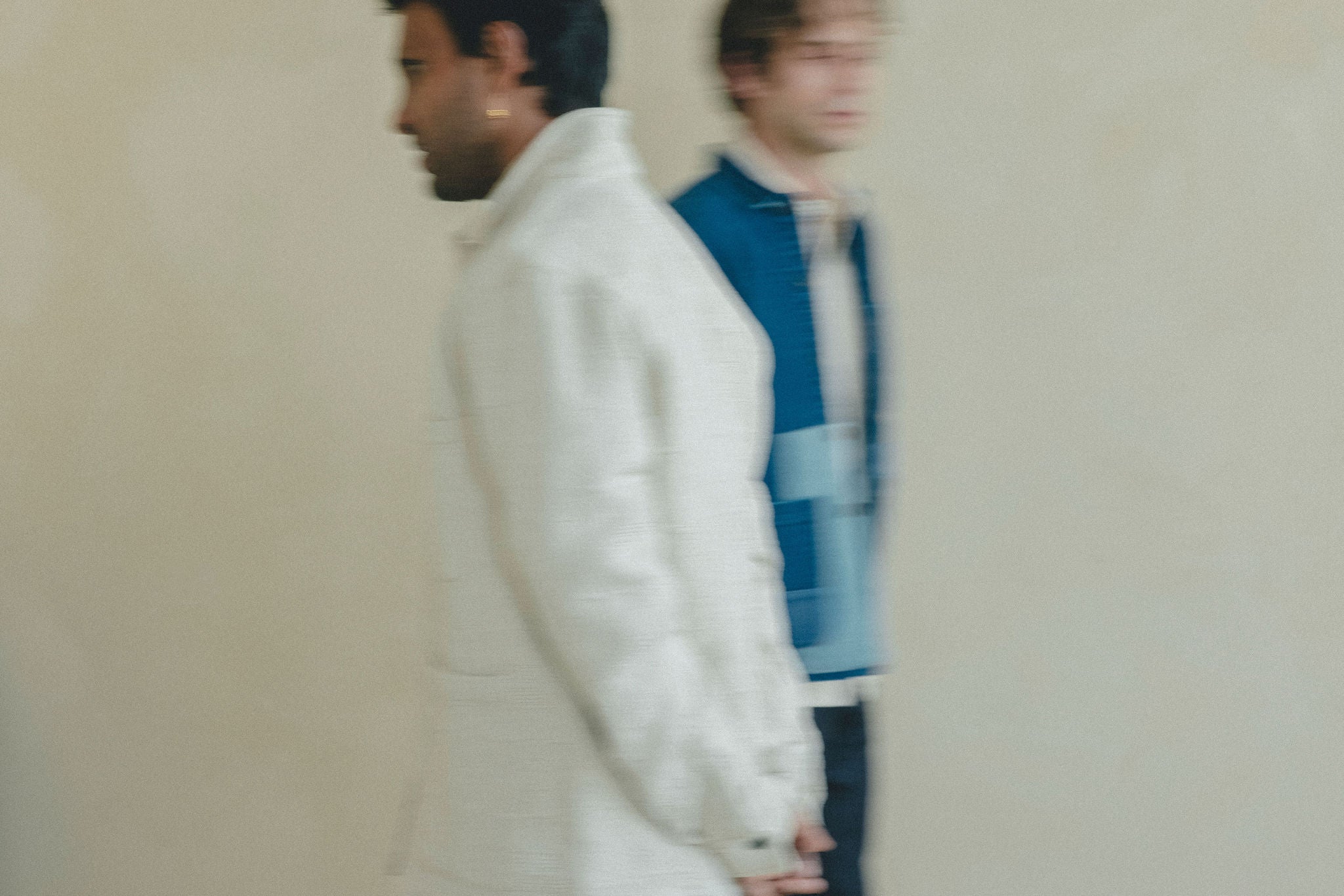 A blurry photo of two men against a neutral background walking by each other