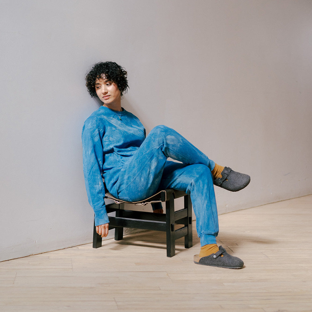 A woman sits in a stool with a full indigo sweatsuit on.