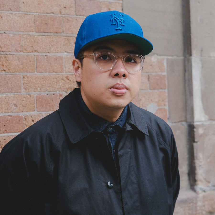 A portrait of a man in a blue Mets cap and black coat.