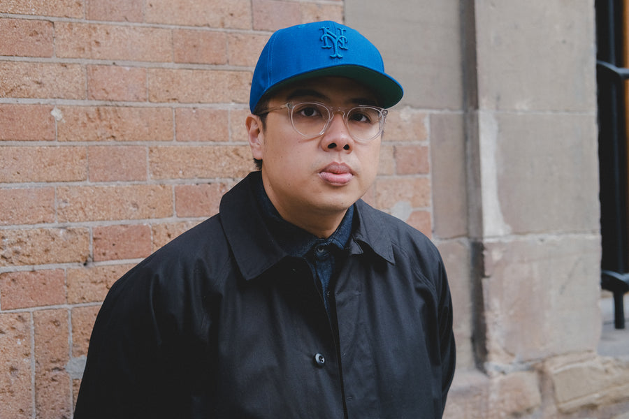 A portrait of a man in a blue Mets cap and black coat.
