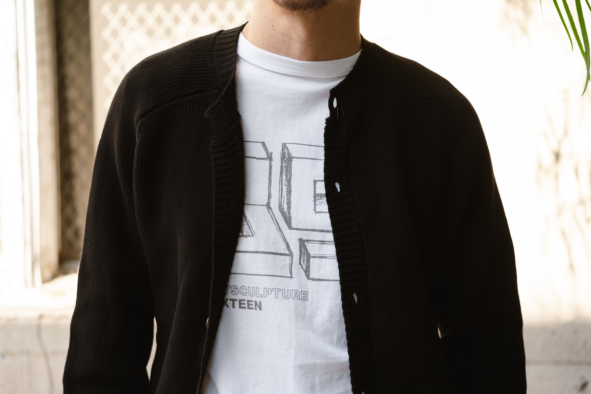 A man wears the Playscapes tee under a black cardigan.