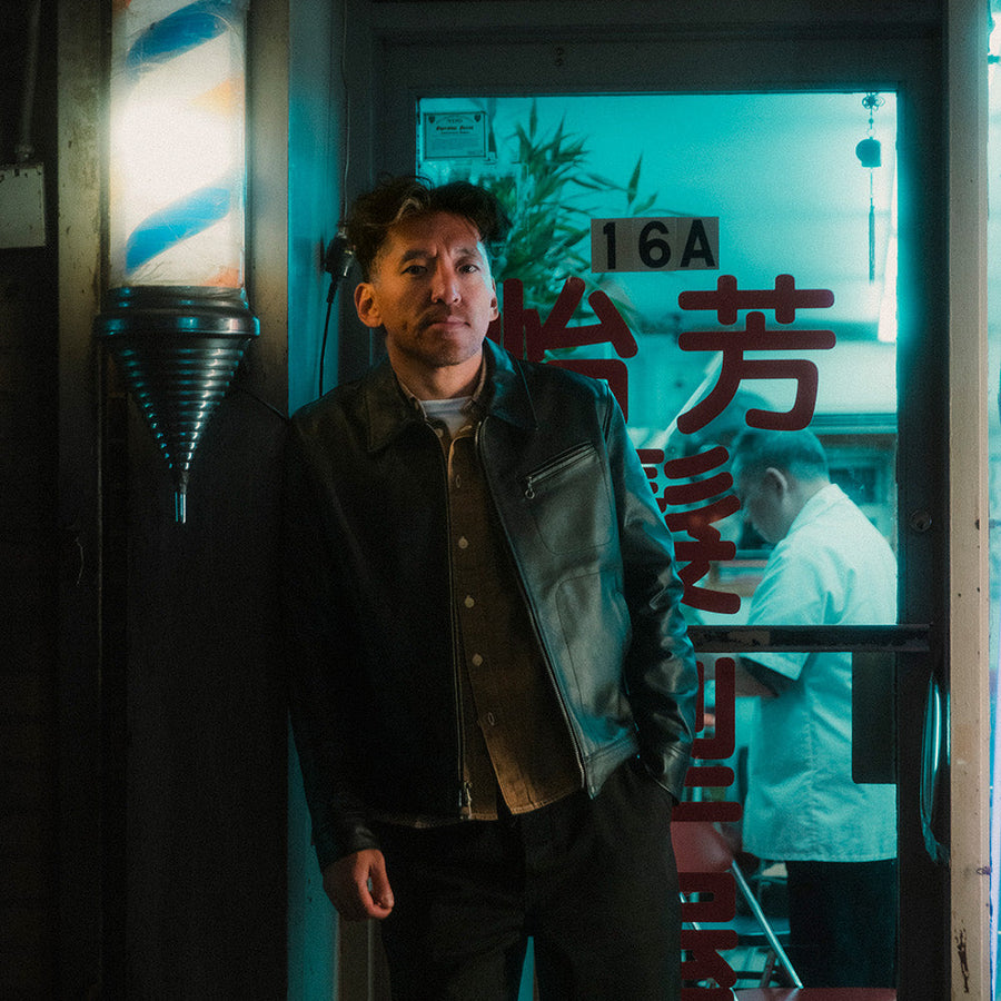 A man in a black jacket stands in front of a barbershop.