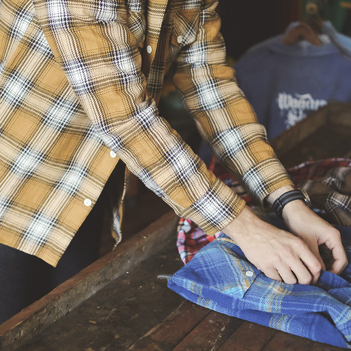 A man in a yellow flannel folds a shirt.