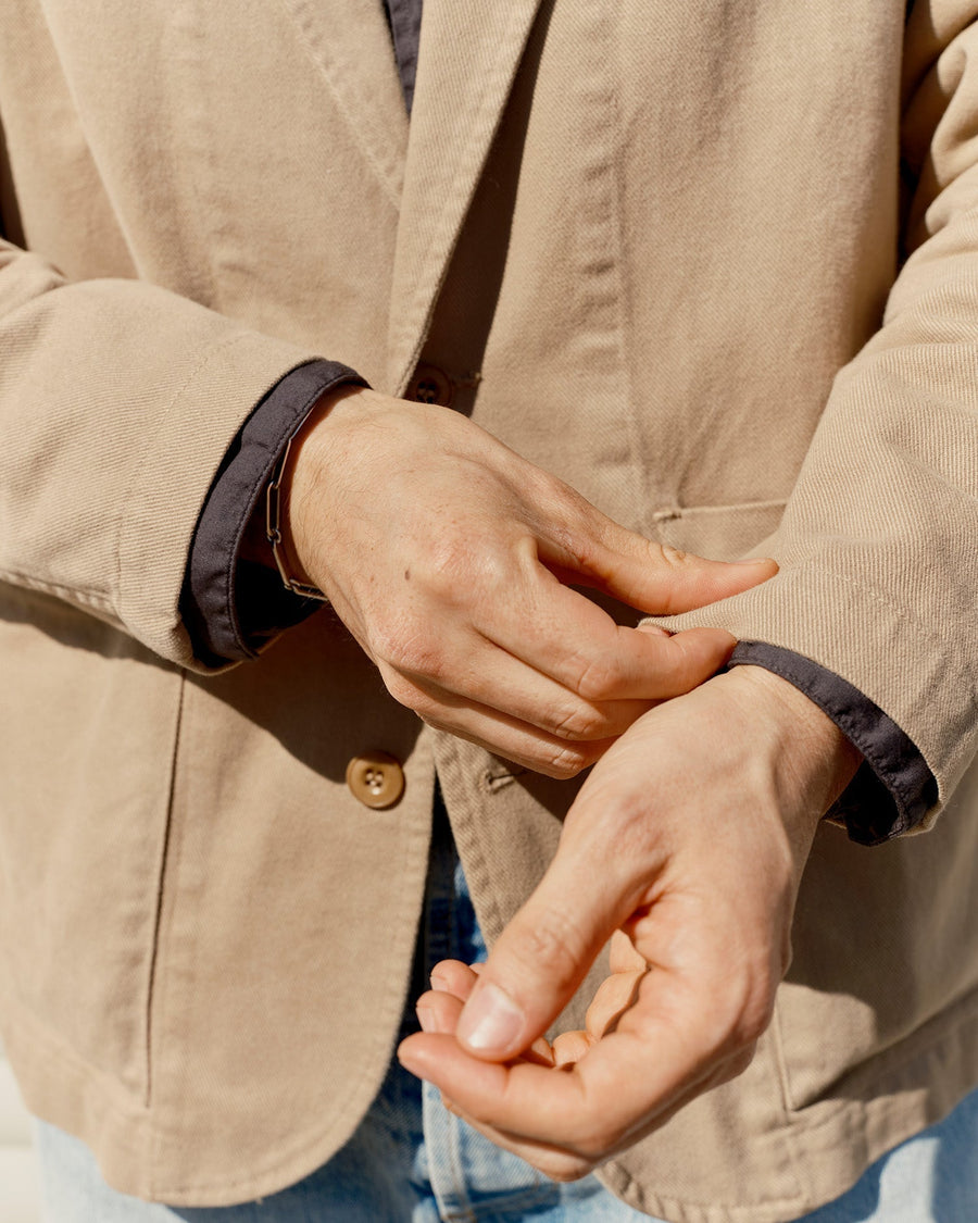 A close up image of a man in a khaki blazer adjusting his cuff.