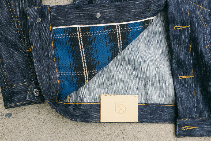 A Type 3s jacket lays on the ground with one corner flipped up to show the flannel pocketbag and natural tan leather patch.