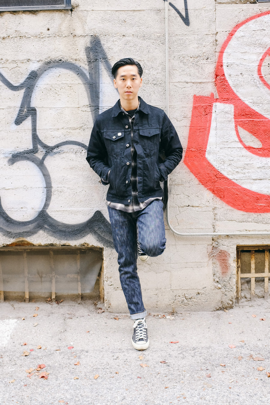 A model leans up against the wall with one leg up, showcasing the 15y denim in the NT fit.