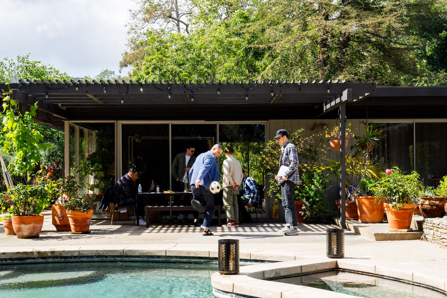 A group of men are standinig around a table while one juggles a soccer ball.