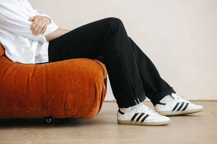 A photo of someone sitting on a red couch in black jeans and white sneakers.