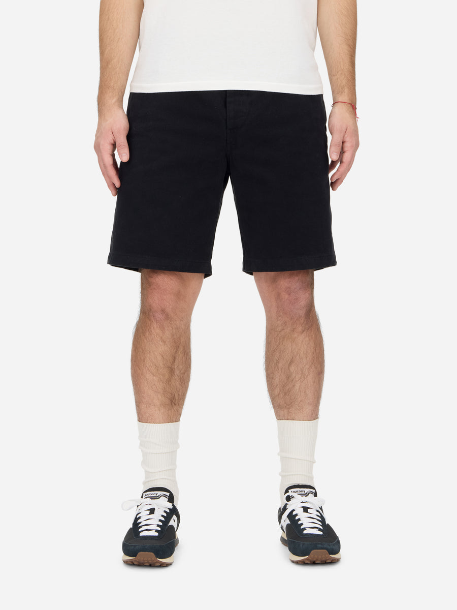A person standing and wearing black safari shorts with a relaxed fit and side buckle waist adjustment, paired with a white t-shirt and white socks.