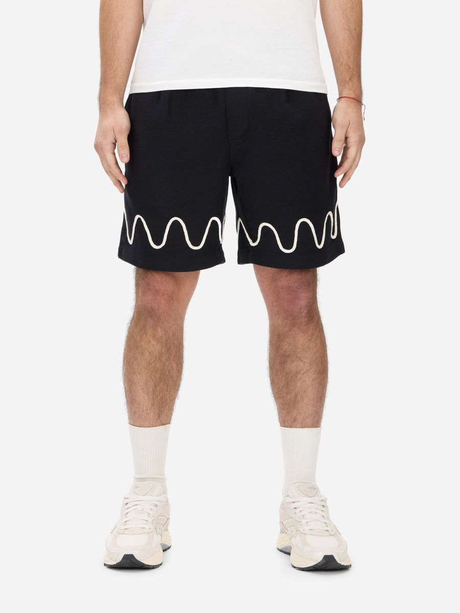 A pair of black soccer shorts with a white squiggle pattern on the hem, featuring an elastic waist with drawstring and front pockets.