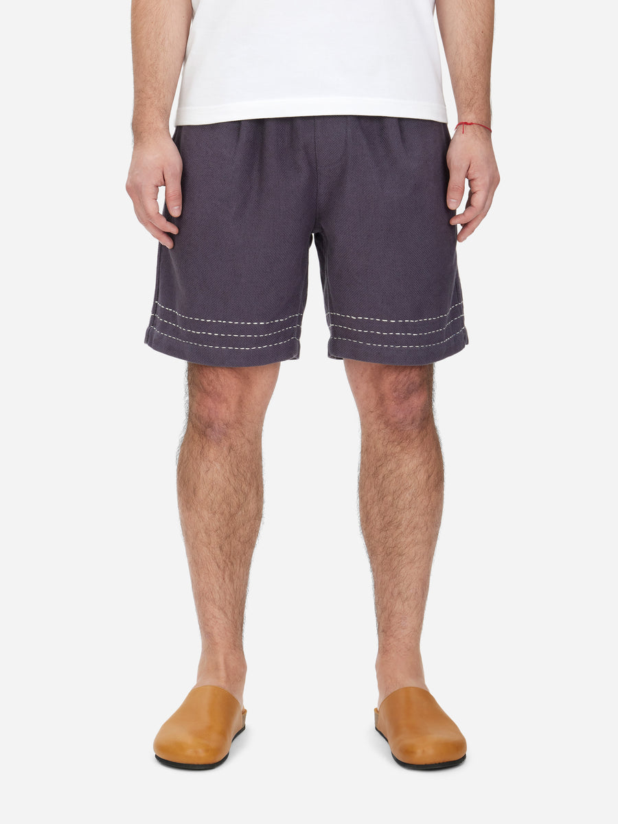 A pair of men's club shorts in a dark color with hand stitching detail around the hem. The shorts have an elastic waist with a drawstring and visible slash front pockets and large rear patch pockets.