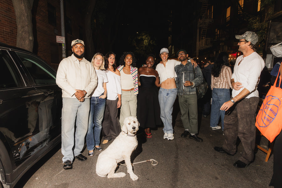 A group of friends stand outside on the street with drinks in hand.