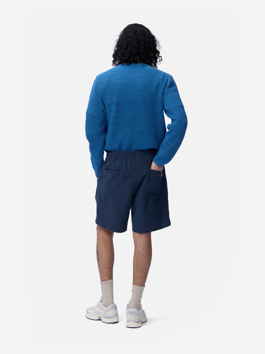 Person wearing a blue sweater and navy shorts on a white background