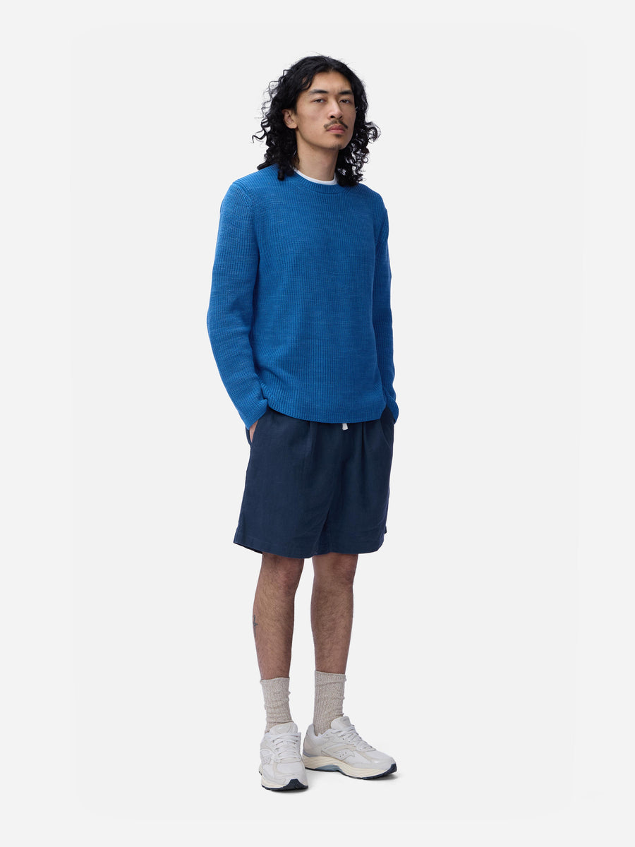 Person wearing a blue sweater and navy shorts on a white background
