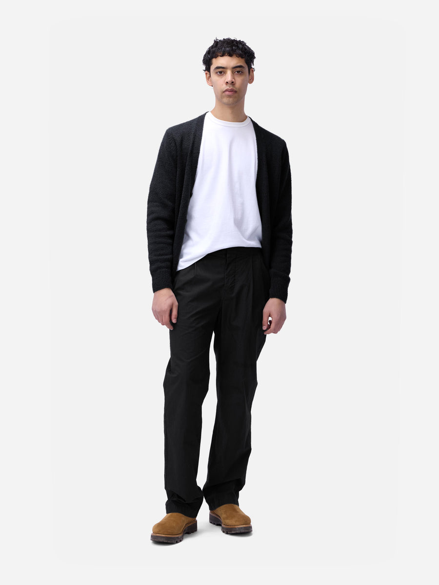 Person wearing a black cardigan, white shirt, black pants, and brown shoes on a white background