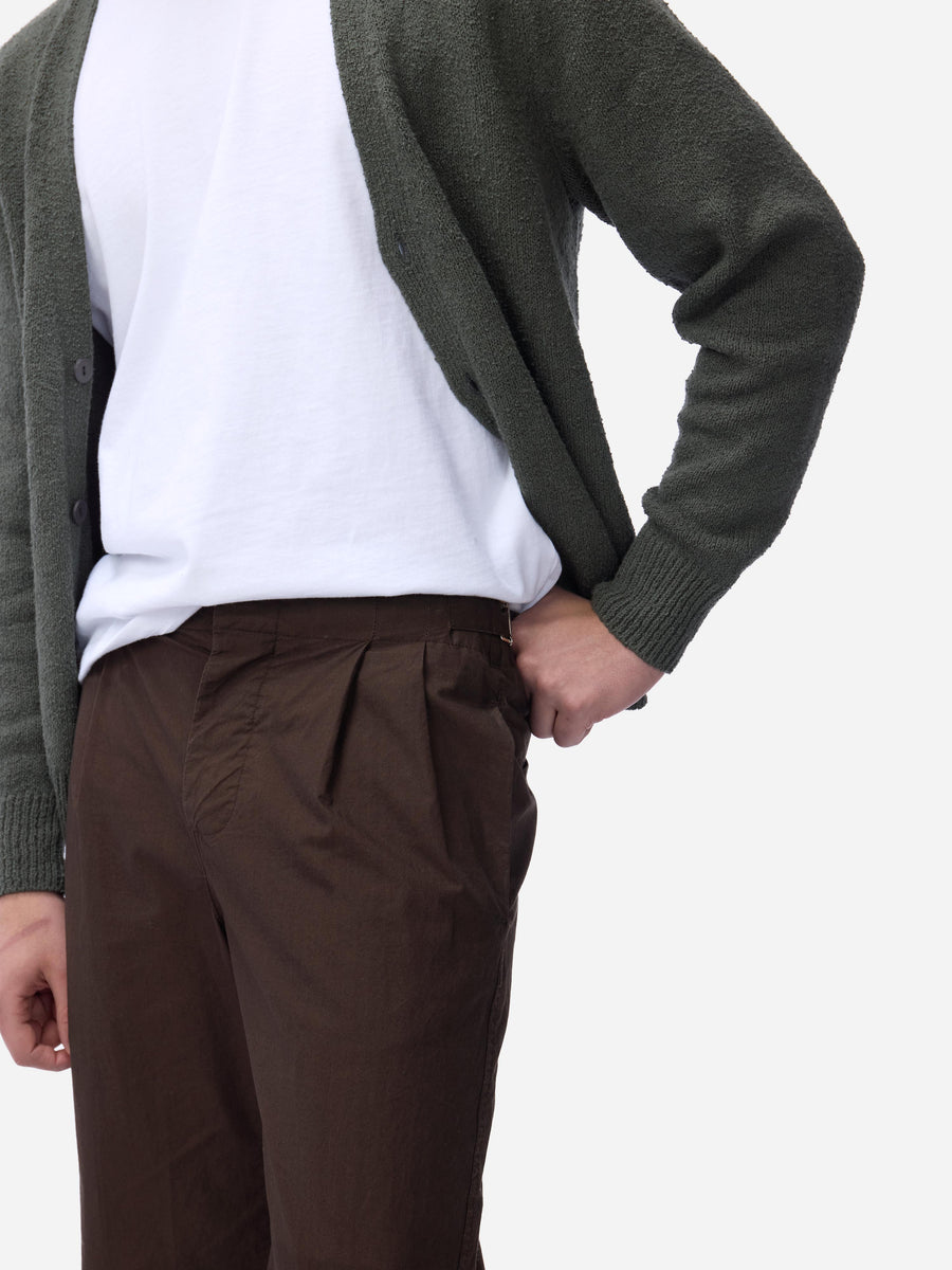 Person wearing a green cardigan, white shirt, and brown pants on a white background