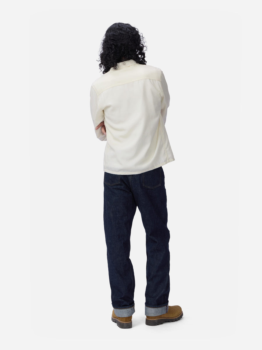 Person wearing a cream shirt and dark jeans on a white background