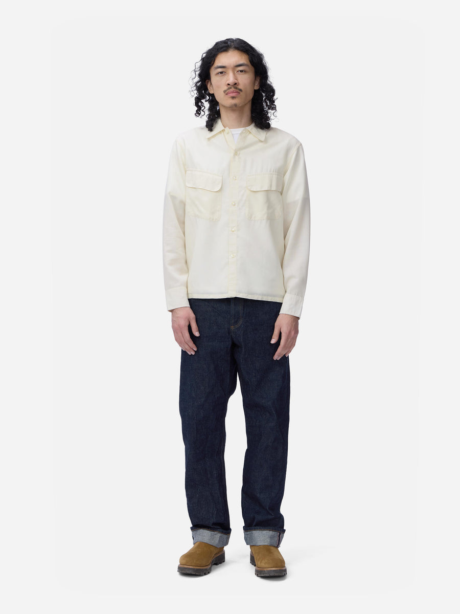 Person wearing a cream shirt and dark jeans on a white background