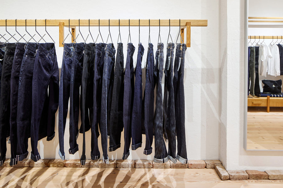 Racks of jeans hanging from a floating wooden rack, with a mirror next to it.
