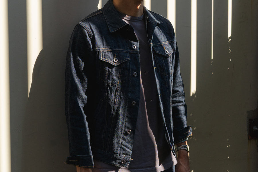 A moody shot of a model wearing a blue denim jacket in shadows.