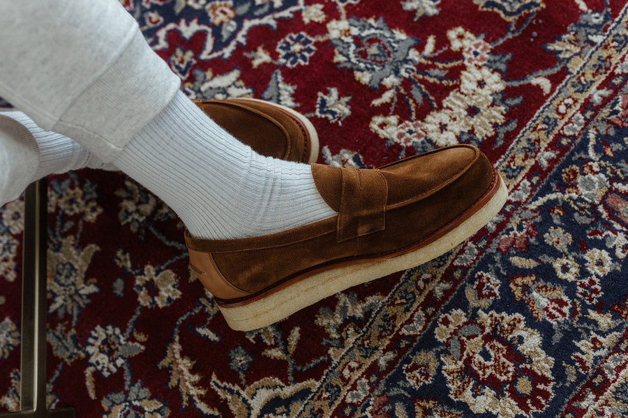 A pair of crossed feat wearing brown loafers on a carpet.