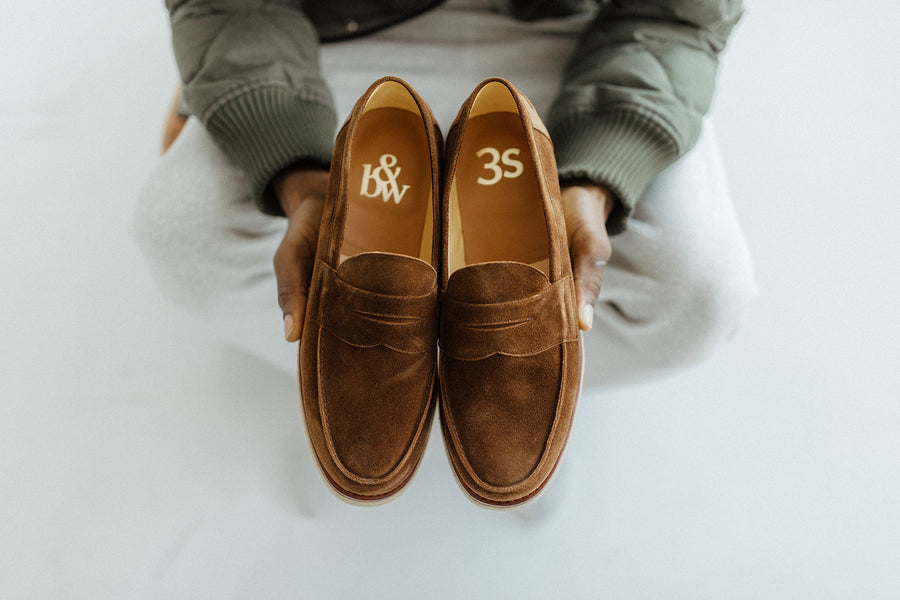 Hands hold a pair of loafers with gold foil brand stampings on the inside of both B&amp;W and 3s.