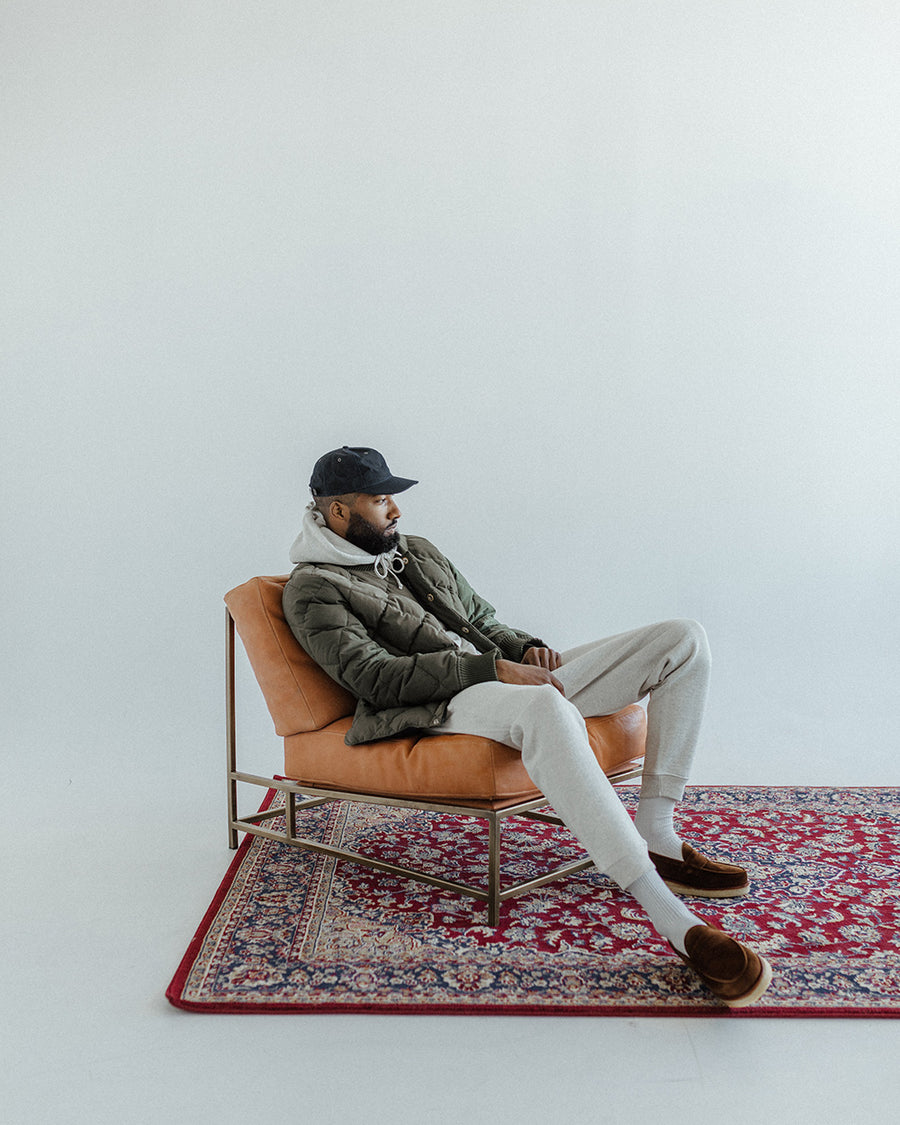 A man wearing loafers sits back in the leather chair on the rug.