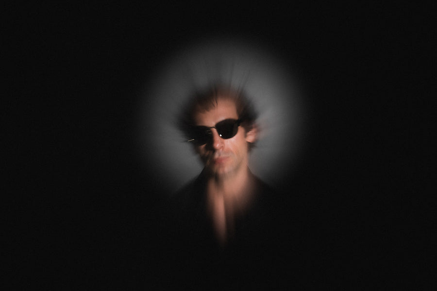 A blurry, hazy photo of a man on a black background wearing sunglasses.