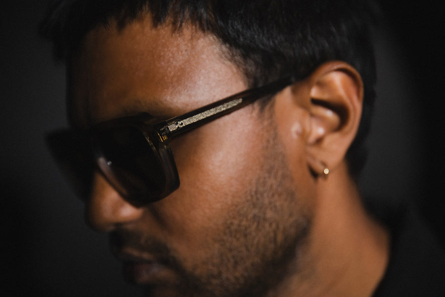 A close up shot of a man wearing a thick pair of acetate sunglasses.
