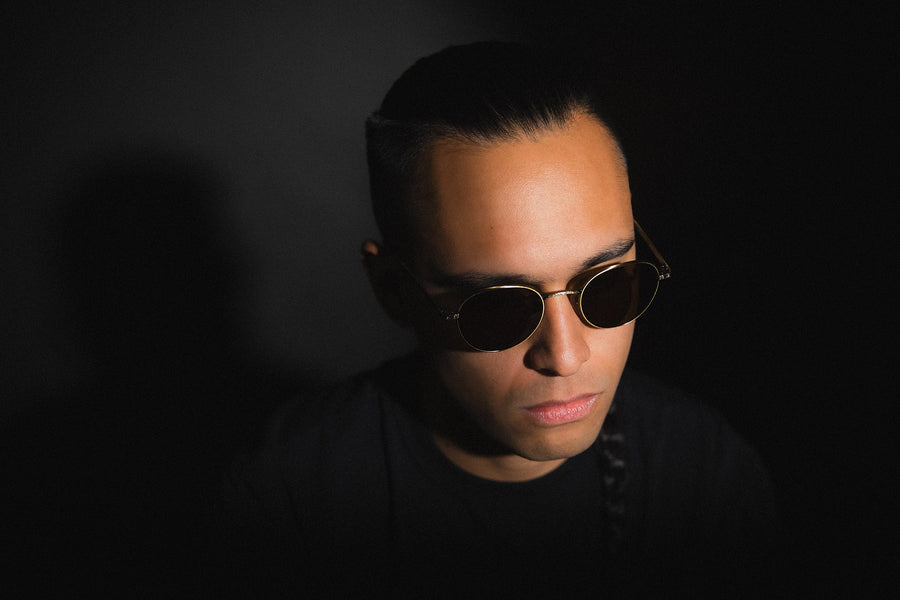 A man wearing round sunglasses against a black background.