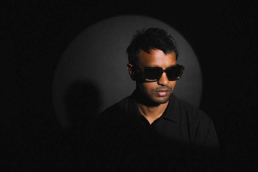 A man wearing thick acetate frames poses in front of a black background.