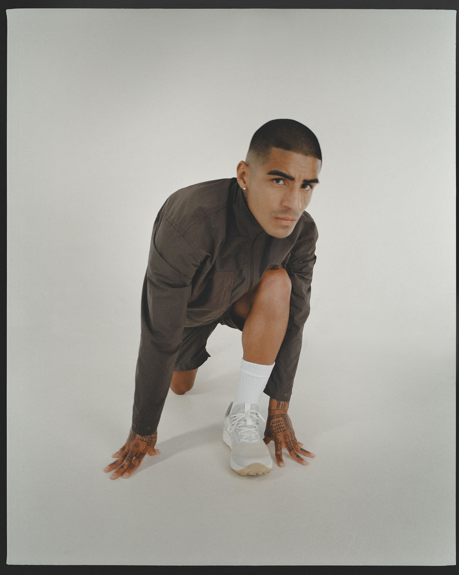 A man stretches with one leg extended far back in a brown nylon shirt.