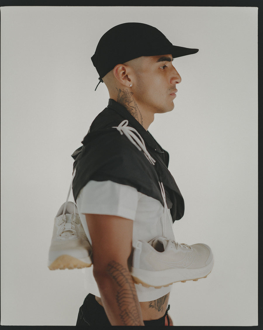 A side profile portrait of a man in a black cap and cropped white tee.