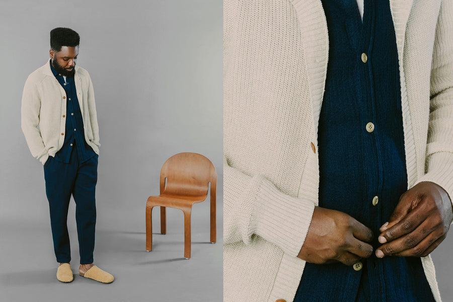 A man in a cream sweater and indigo pants looks down at the floor.