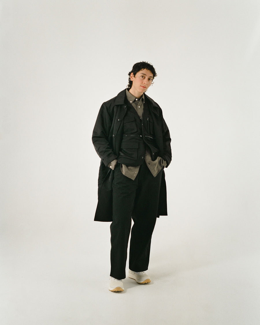 A woman wears a dark brown shirt, black nylon vest and black nylon long coat.