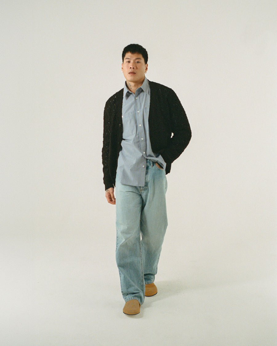 A man in a blue striped shirt and black cardigan walks forward.