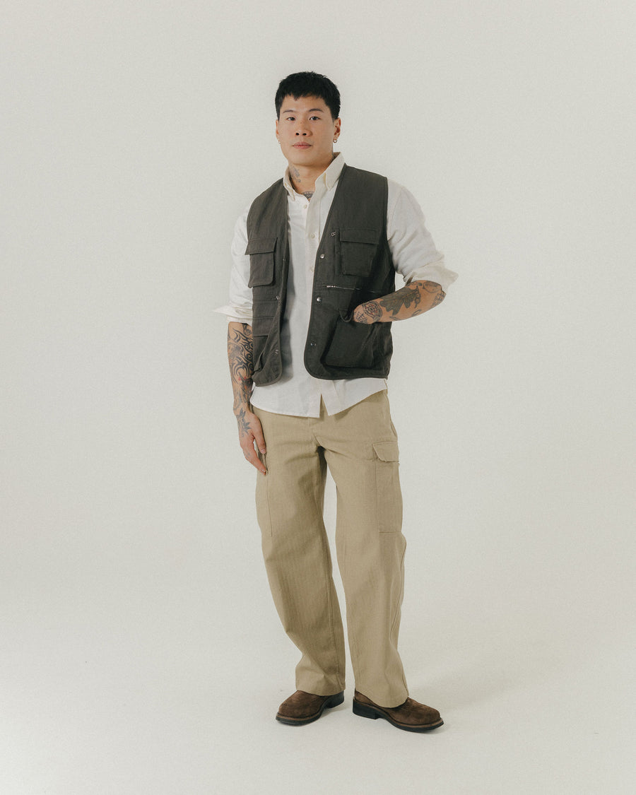 A man in a white shirt and olive vest paired with tan cargo pants looks like Indiana Jones.