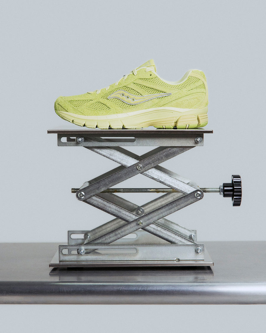 A neon yellow sneaker on a scientific metal pedestal.