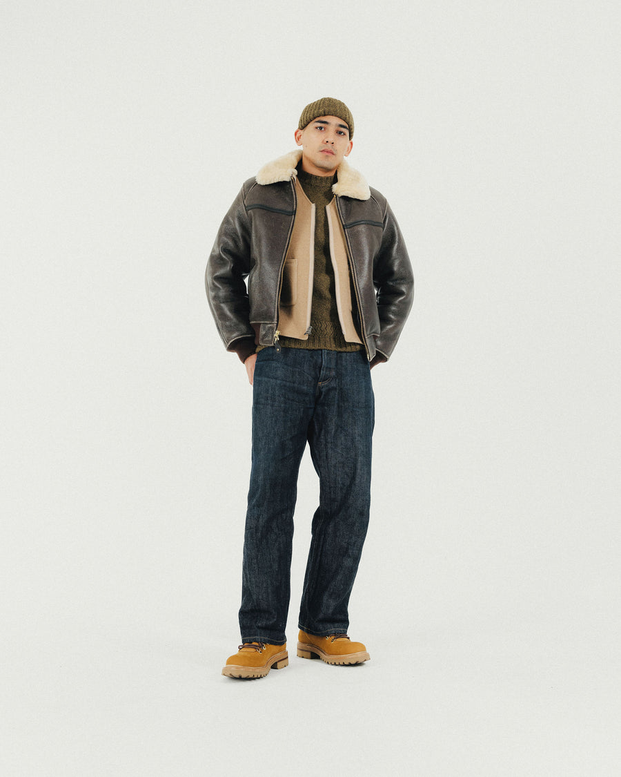 A man in a knit cap and leather shearling bomber looks into the camera.