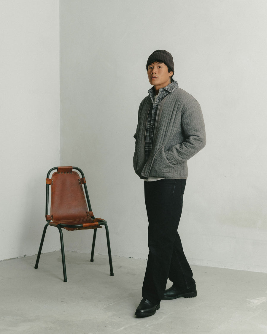 A man in a grey quilted liner jacket and black jeans strolls across the frame.