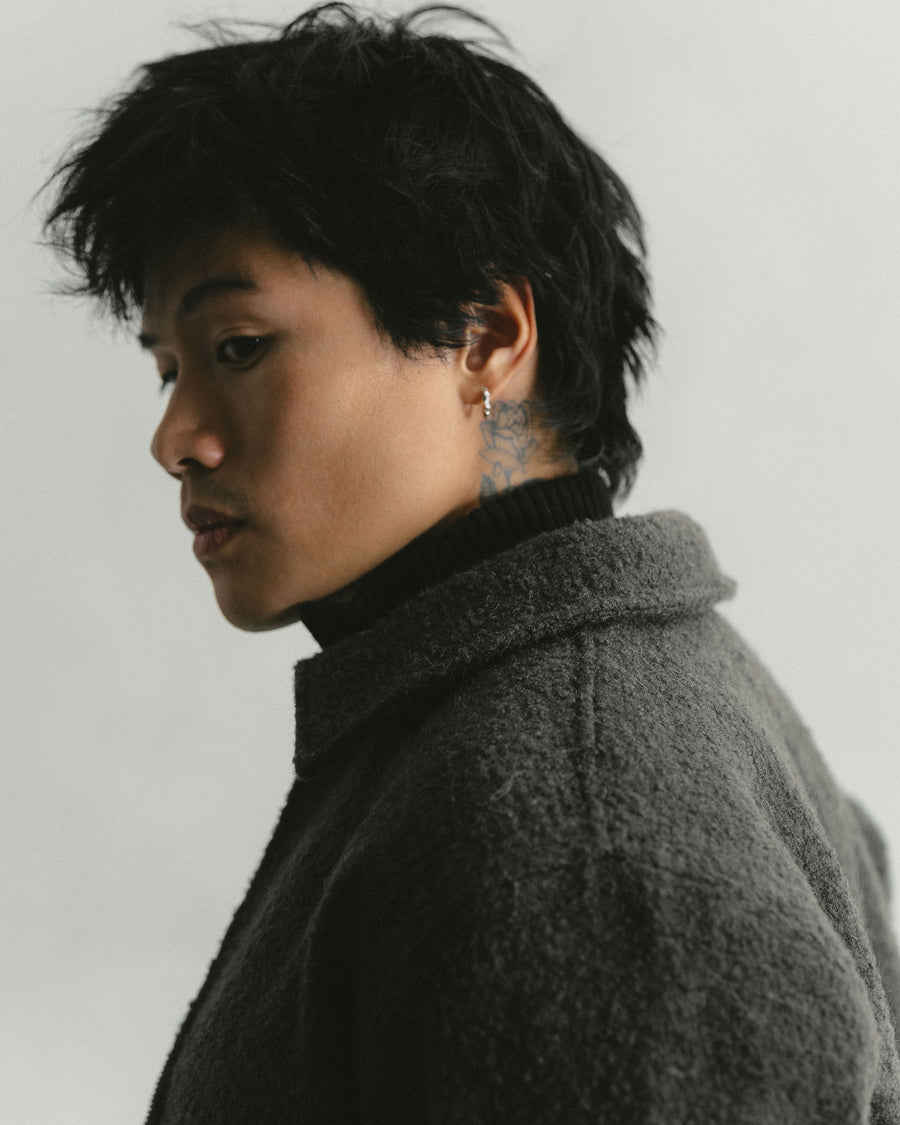 A close up side profile portrait of a man in a grey wool jacket.