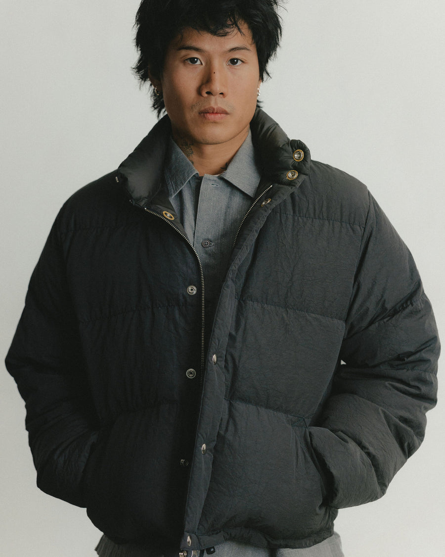 A portrait of a man wearing a puffy black down jacket over a grey button down shirt.