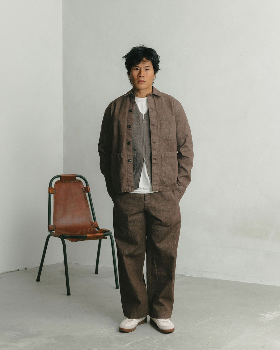 A man in a brown denim matching jacket and pant poses in front of a leather chair.